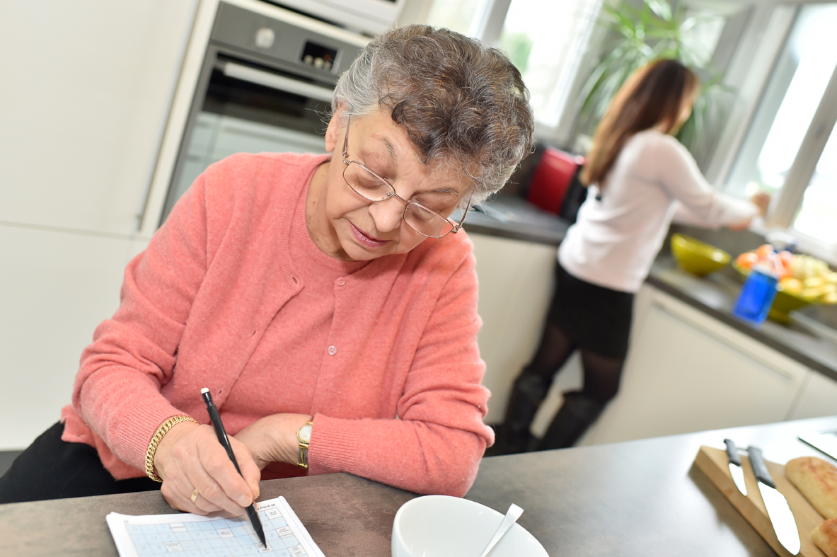 Elderly woman doing crosswords while homecare helps at home